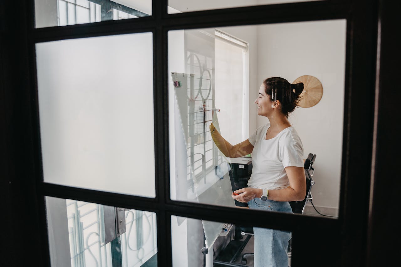 Woman writing on a whiteboard in a modern office, smiling and focused.
