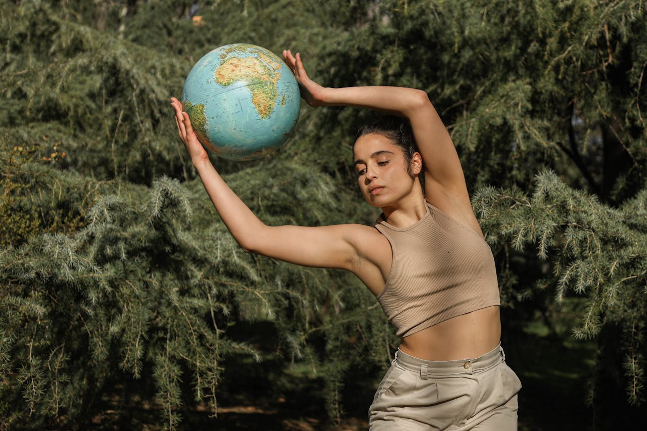 A woman gracefully poses with a globe amidst lush greenery, symbolizing environmental awareness.